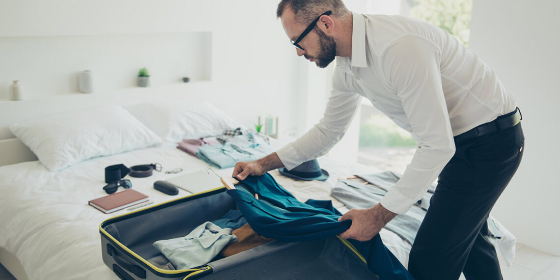 Man folding a suit jacket for travel next to a travel jacket.